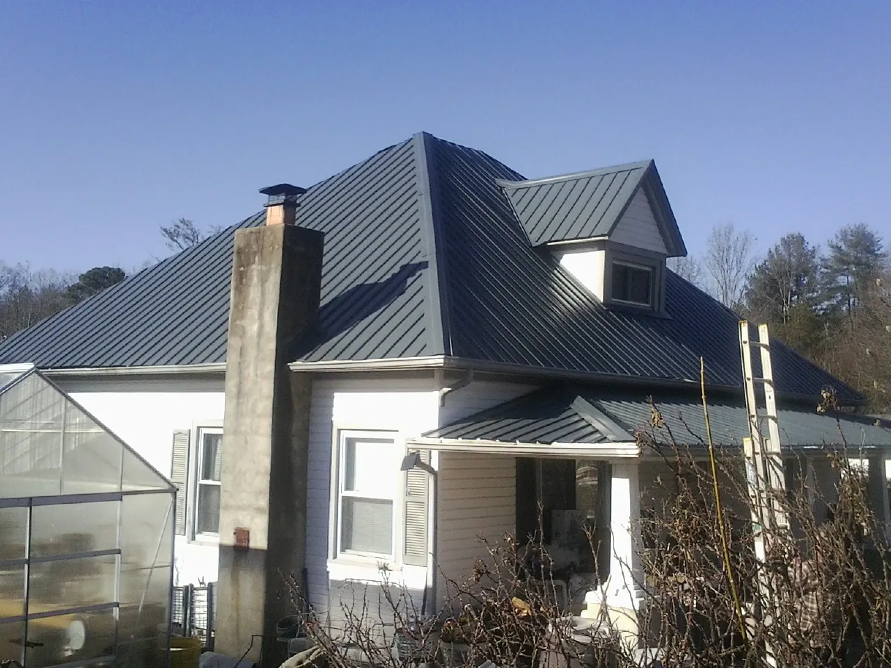 Dark blue standing seam metal roof on a white farmhouse with dormer — Slate & Tile Roof Repair by Roofing Brothers in San Antonio