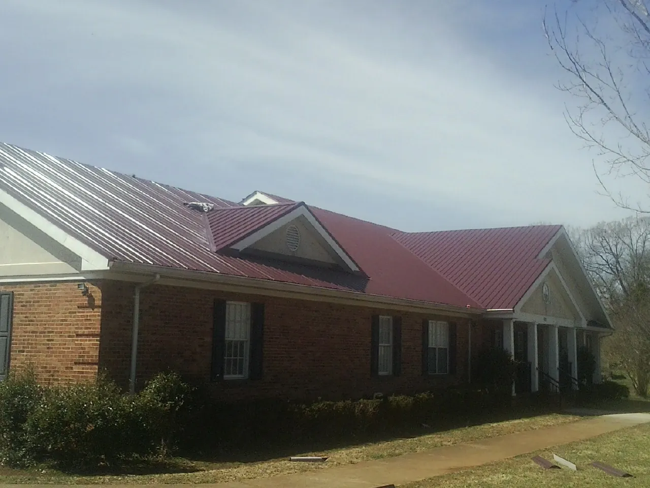 Red metal roof with gabled entries on a long brick building, from a Hail Damage Roof Repair job in San Antonio