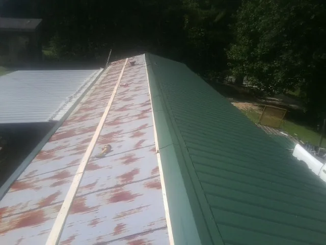 Old rusted panels beside newly installed green metal roofing in San Antonio