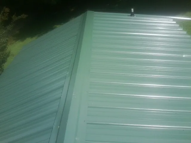 New green metal panels meeting at the ridge of a roof — Flat Roof Repair work by our crew in San Antonio